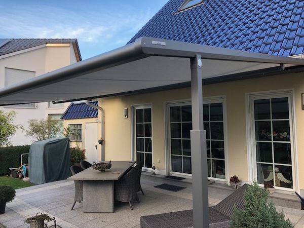 Moderne Terrassenüberdachung aus Aluminium mit Markise an Einfamilienhaus im Garten.