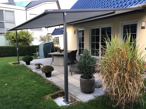Überdachte Terrasse mit Markise, modernen Gartenmöbeln und großen Pflanzkübeln im Garten.