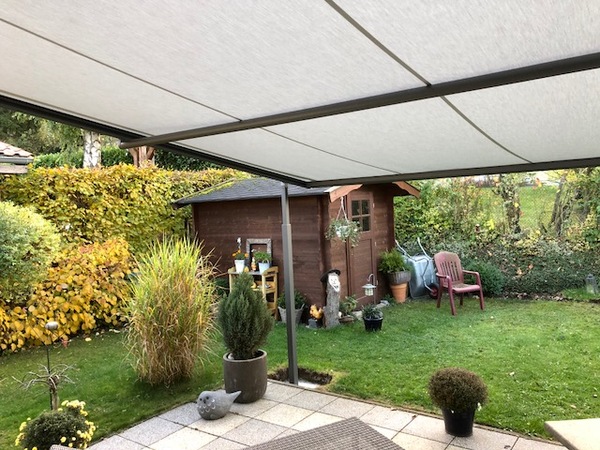 Überdachte Terrasse mit Blick auf gepflegten Garten und Holzhaus im Hintergrund.