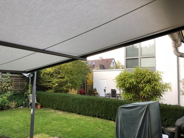 Moderne Terrassenüberdachung im Garten mit Blick auf gepflegten Rasen und Hecke.