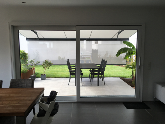 Große Terrassentür mit Blick auf moderne überdachte Terrasse und Garten mit Gartenmöbeln.