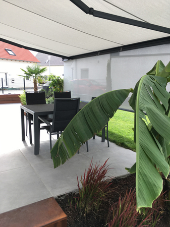 Moderne Terrasse mit Markise, Gartenmöbeln und exotischen Pflanzen im gepflegten Garten.