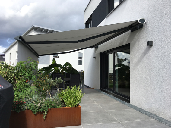 Moderne Terrasse mit Markise am Einfamilienhaus, Sitzbereich und Pflanzkübel im Garten.